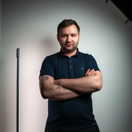 Portrait of a confident man with tattoos standing in a studio, arms crossed.