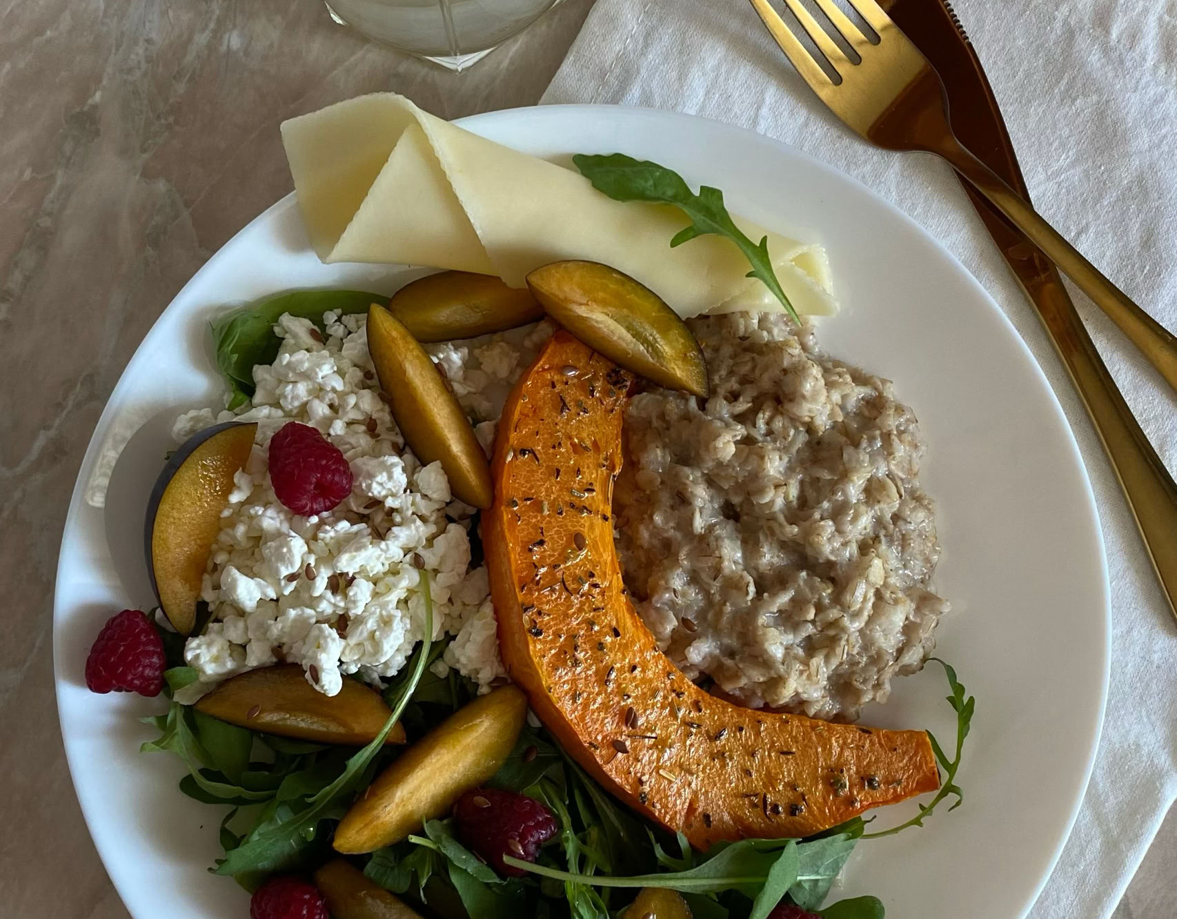A nutritious plate with quinoa, roasted pumpkin, arugula, cheese, and fruit, served with lemon water.