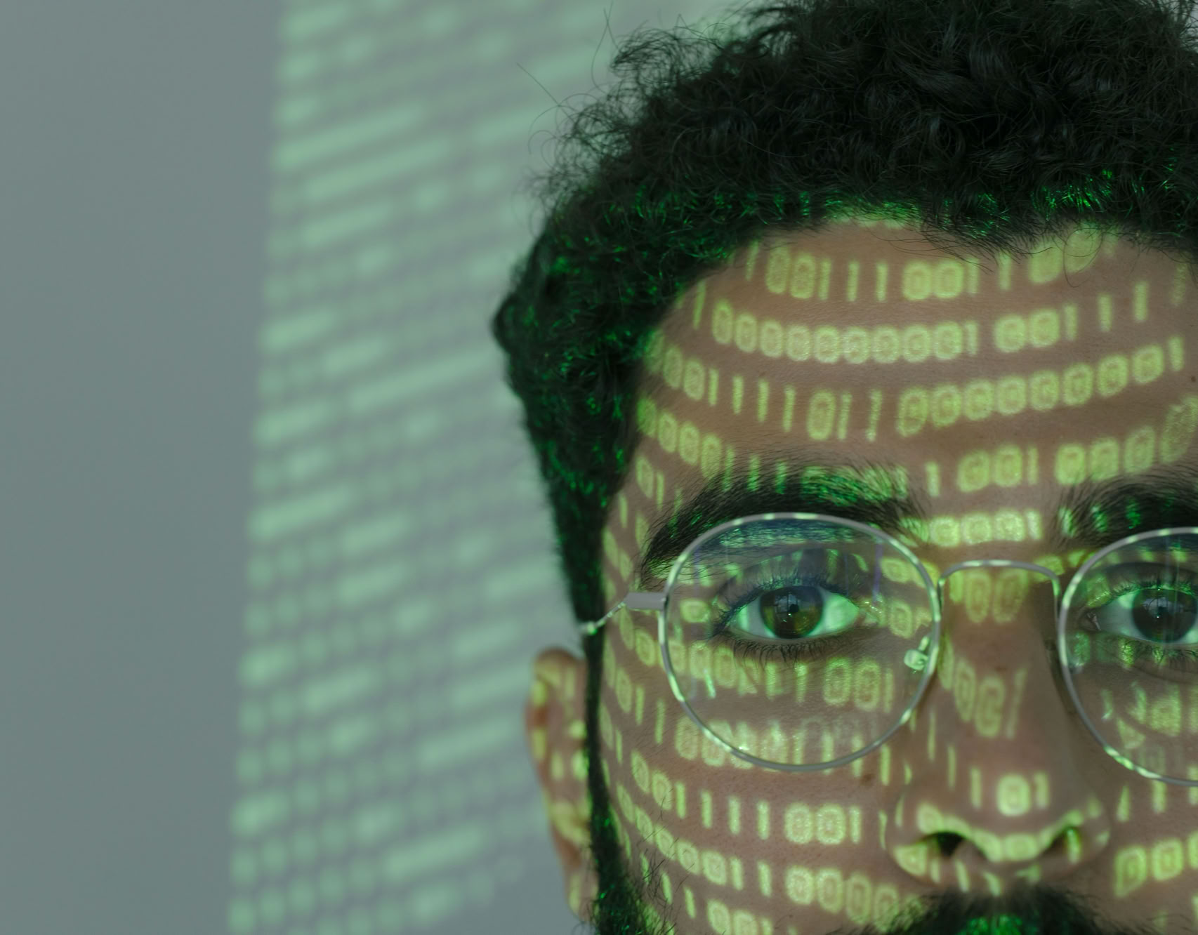 Close-up of a man with binary code projected on his face, symbolizing cybersecurity.